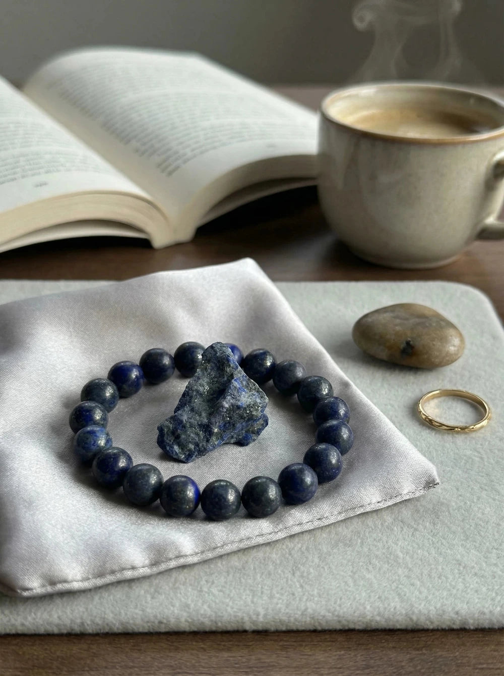 Zilā lazurīta (Lapis Lazuli) dabīgo akmeņu pērlīšu aproce un neapstrādāts kristāls uz satīna maisiņa, MARREdeco juvelierizstrādājumu kolekcija