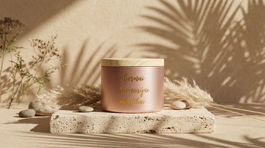 MARREdeco sojas vaska svece rozā zelta traukā ar koka vāciņu un zelta uzrakstu "iedvesmai, harmonijai, mīlestībai", novietota uz akmens pamatnes siltā saules gaismā.