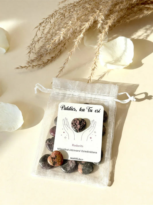 Rodonīta sirds uz kartītes baltā organzas maisiņā kopā ar vairākām rodonīta sirsniņām uz gaiša fona, marredeco