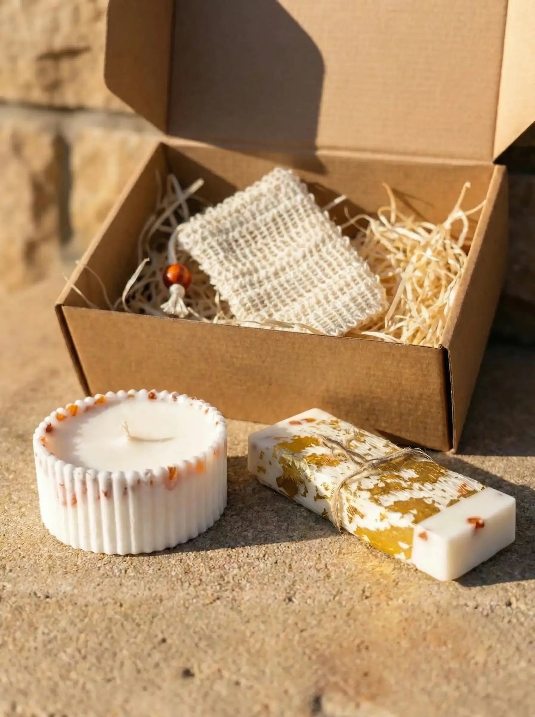 MarreDeco dāvanu komplekts ar rievotu sveci, vaska plāksnīti un dzintariem, izkārtots uz akmens virsmas blakus atvērtai eko iepakojuma kastei.
