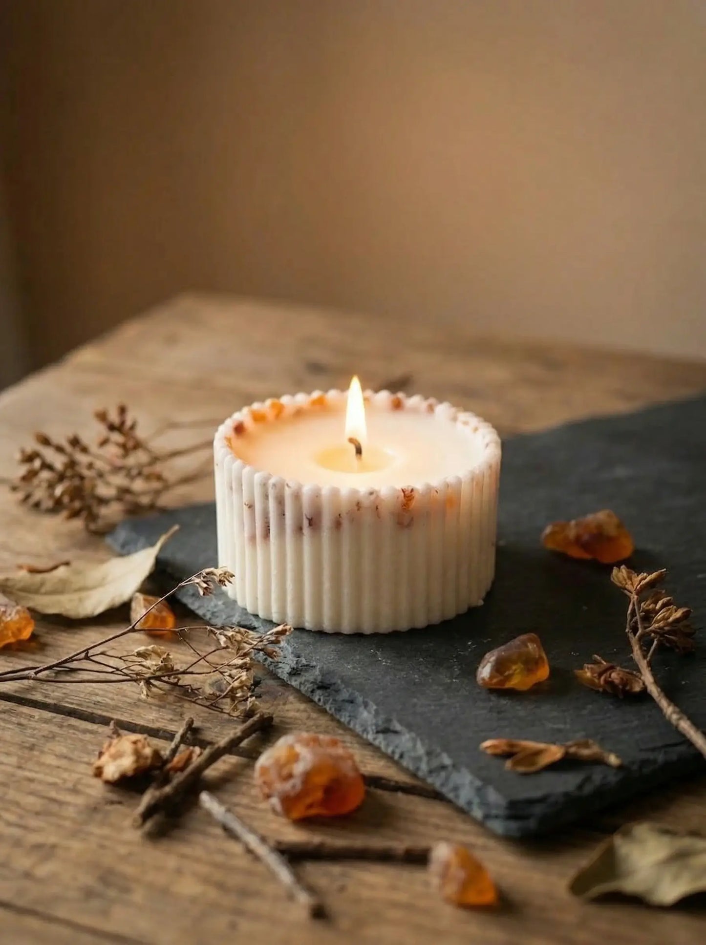MarreDeco degoša, rievota dizaina svece ar iestrādātiem dzintara gabaliņiem, novietota uz pelēkas akmens plāksnes mājīgai atmosfērai.