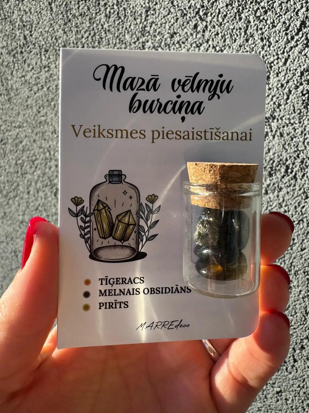 MarreDeco "Mazā vēlmju burciņa" veiksmes piesaistīšanai ar tīģeraci, ametistu un zaļo avanturīnu, turēta rokā pret pelēku fonu.