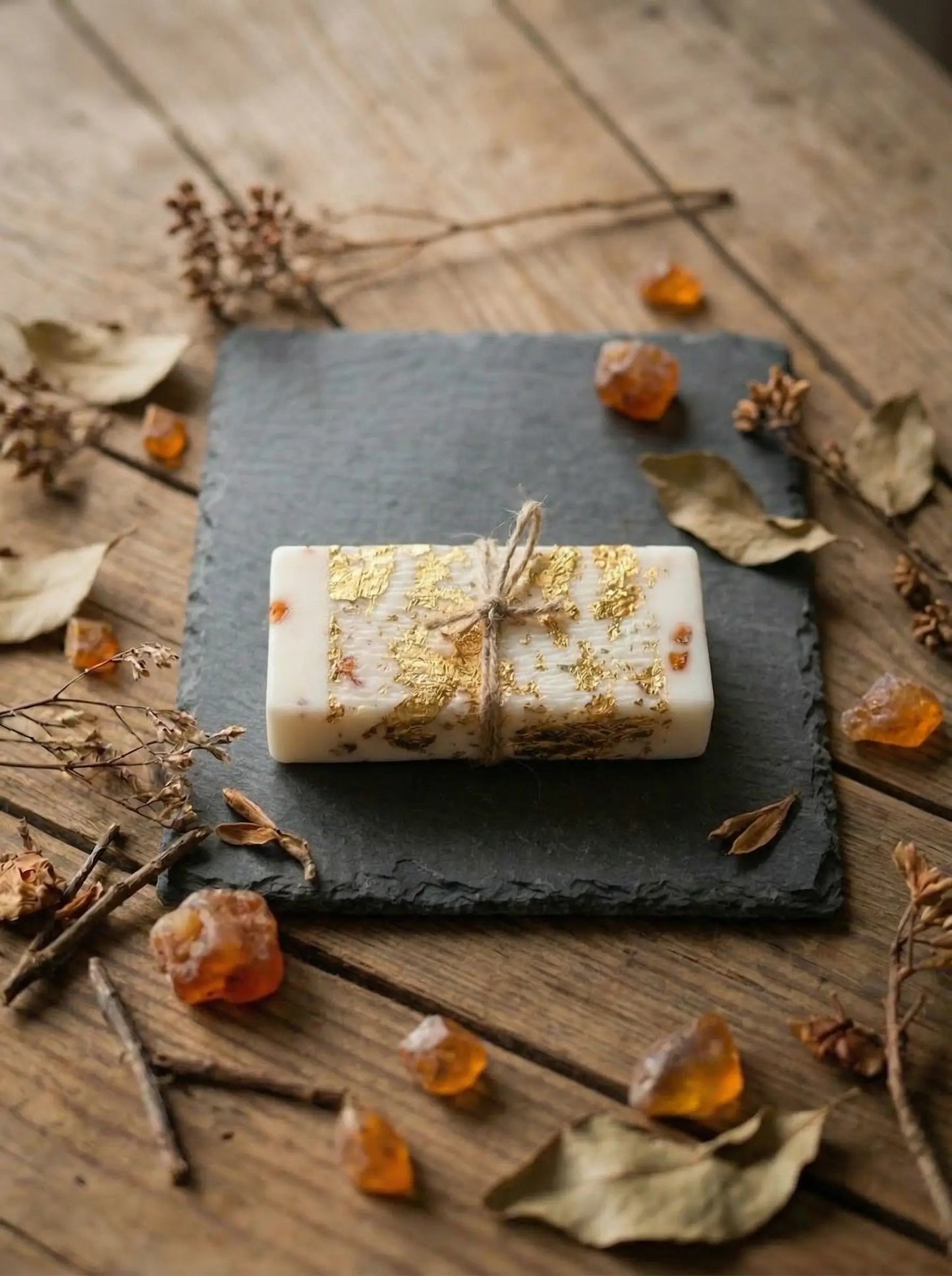 MarreDeco dabīgās kazas piena ziepes ar iestrādātiem dzintara gabaliņiem un zelta folijas dekoru, apsietas ar linu aukliņu uz akmens paliktņa.