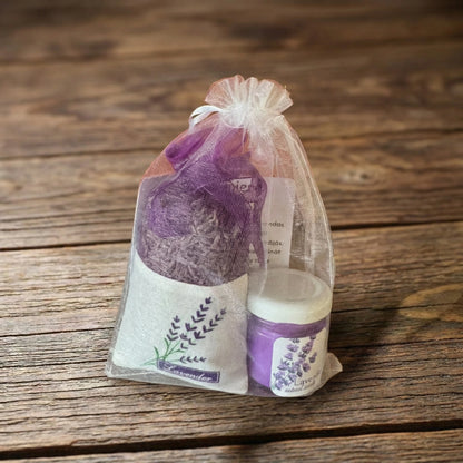 Iepakots lavandas dāvanu komplekts baltā organzas maisiņā, kurā redzama violeta svece stikla burciņā un aromātiskais lavandas ziedu maisiņš