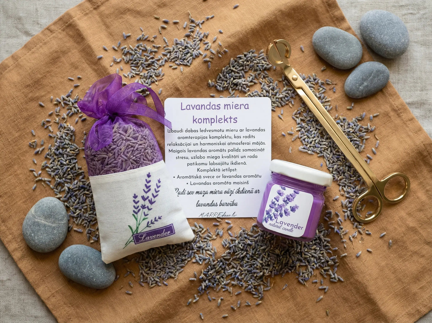 Lavandas miera dāvanu komplekts ar violetu kristālisko palmu vaska sveci, kaltētu lavandas ziedu maisiņu un kartīti uz brūna auduma fona ar dekoratīviem akmeņiem.