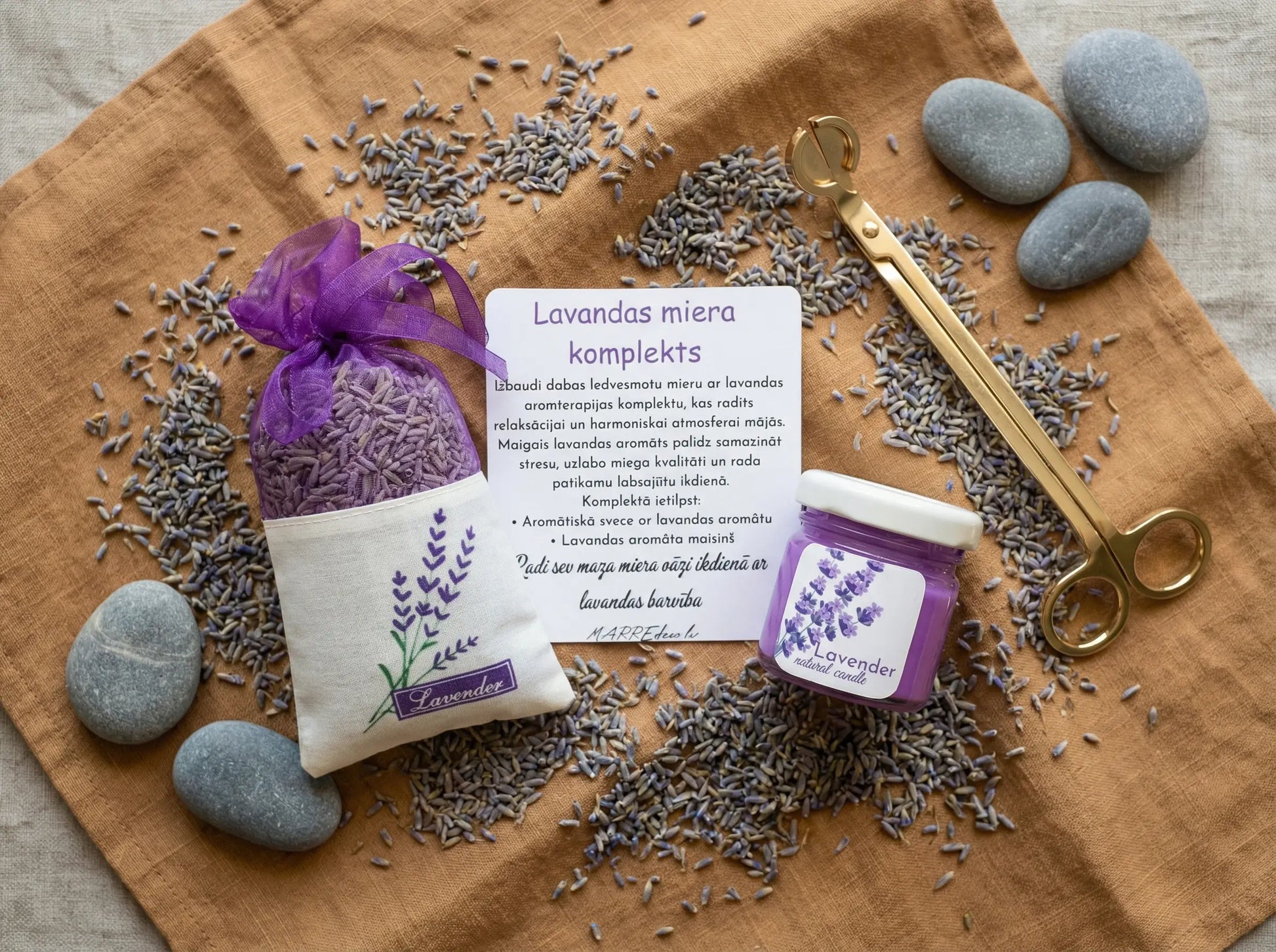 Lavandas miera dāvanu komplekts ar violetu kristālisko palmu vaska sveci, kaltētu lavandas ziedu maisiņu un kartīti uz brūna auduma fona ar dekoratīviem akmeņiem.