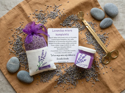 Lavandas miera dāvanu komplekts ar violetu kristālisko palmu vaska sveci, kaltētu lavandas ziedu maisiņu un kartīti uz brūna auduma fona ar dekoratīviem akmeņiem.