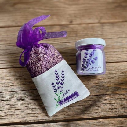 Lavandas aromterapijas komplekts uz koka virsmas: lina maisiņš ar kaltētiem lavandas ziediem un violeta palmu vaska svece stikla burciņā.