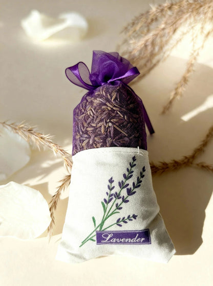 Auduma maisiņš pildīts ar kaltētiem lavandas ziediem, dekorēts ar lavandas izšuvumu un violetu organzas lenti uz gaiša fona, marredeco