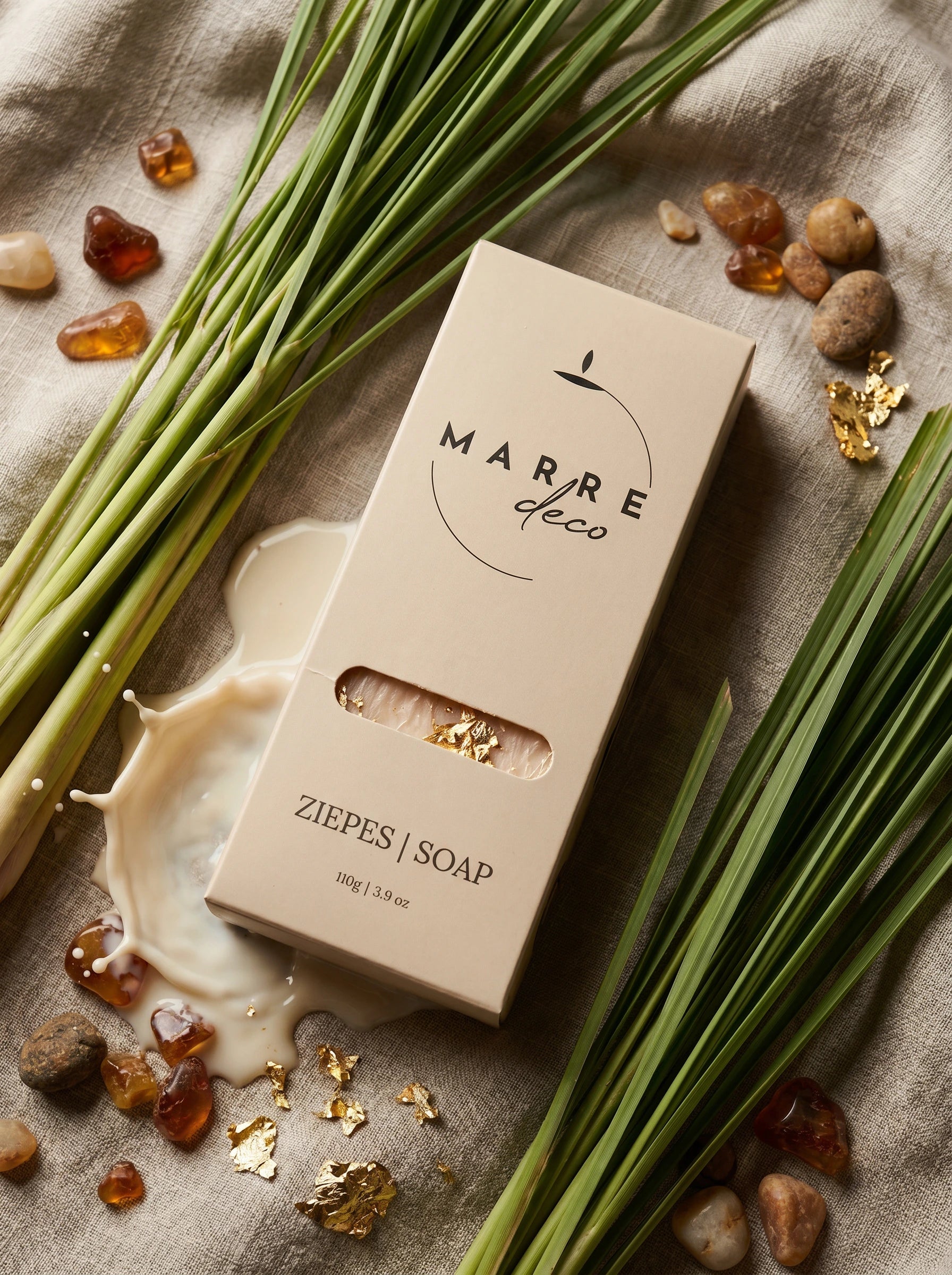 Ekskluzīvas roku darba kazas piena ziepes ar dzintaru un zeltu — zīmola MarreDeco produkta iepakojums estētiskā dabas kompozīcijā.
