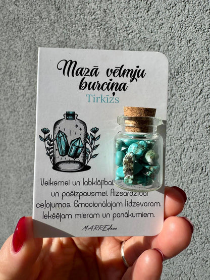 MarreDeco "Mazā vēlmju burciņa" ar tirkīza akmeņiem veiksmei, labklājībai un aizsardzībai ceļojumos, turēta rokā uz pelēka fona