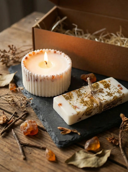 Dāvanu komplekts ar degošu rievotu sveci un vaska plāksnīti, kas dekorēta ar zelta foliju un dzintara gabaliņiem uz akmens pamatnes.