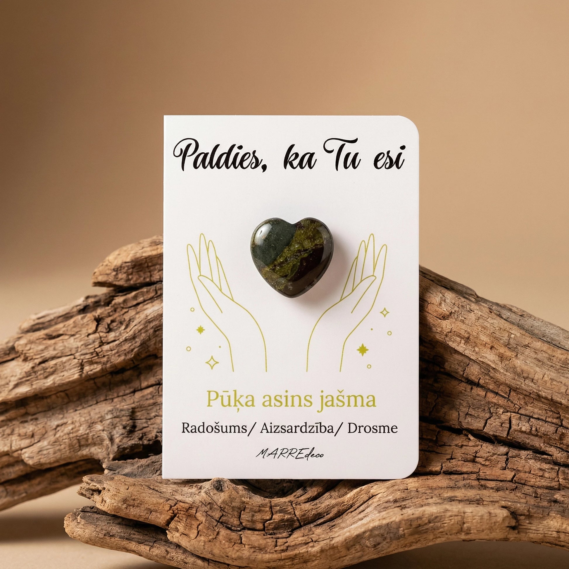 Pūķa asins jašmas sirds formas akmens tumši zaļos un sarkanos toņos uz baltas kartītes ar uzrakstu "Paldies, ka Tu esi" un nozīmi "Radošums / Aizsardzība / Drosme". Kartīte novietota uz dabiska koka zara