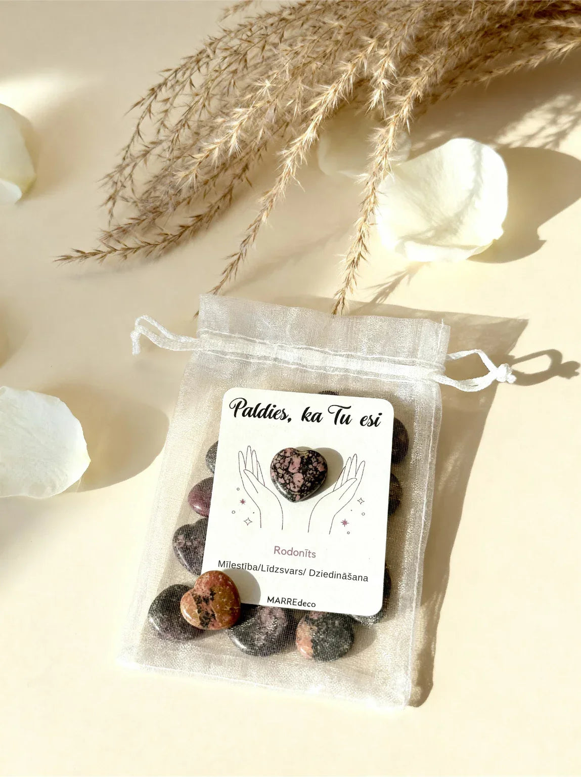 Rodonīta sirds uz kartītes baltā organzas maisiņā kopā ar vairākām rodonīta sirsniņām uz gaiša fona, marredeco