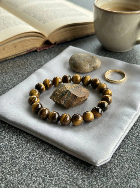 MARREdeco brūnā tīģeracs (Tiger Eye) dabīgo akmeņu pērlīšu aproce un neapstrādāts tīģeracs kristāls uz pelēka satīna auduma