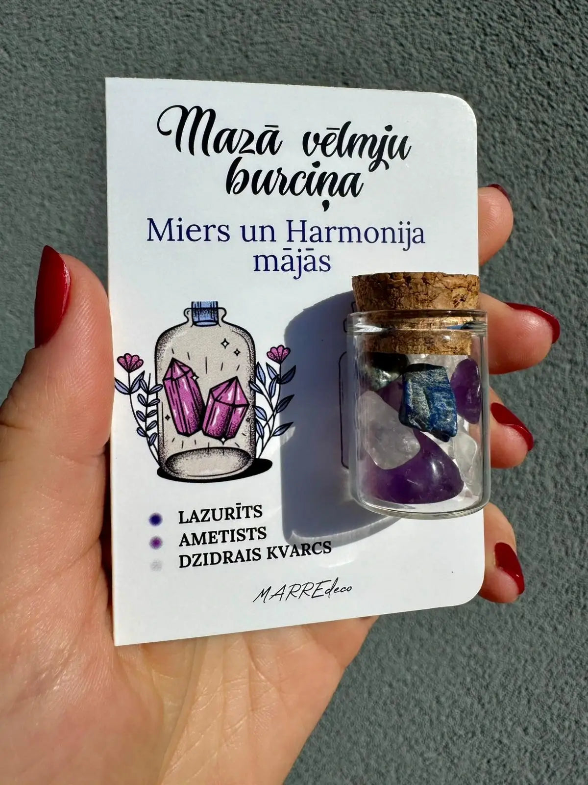 MarreDeco "Mazā vēlmju burciņa" mieram un harmonijai ar lazurīta, ametista un dzidrā kvarca kristāliem, turēta rokā pret neitrālu fonu.