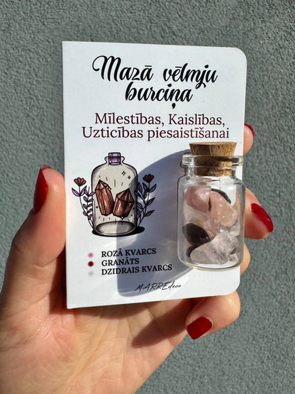 MarreDeco "Mazā vēlmju burciņa" mīlestības un kaislības piesaistīšanai ar rozā kvarca, granāta un dzidrā kvarca kristāliem, turēta rokā.